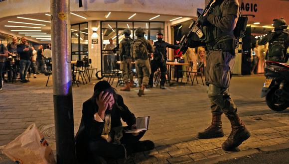 Un hombre judío ultraortodoxo reacciona mientras sostiene un volumen del Libro de los Salmos mientras las fuerzas de seguridad se reúnen detrás de un restaurante en la escena de un ataque a tiros en la calle Dizengoff en el centro de la ciudad costera mediterránea de Tel Aviv en Israel el 7 de abril de 2022. (Foto de AHMAD GHARABLI / AFP)