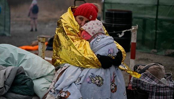 Una mujer abraza a su nieta mientras la gente espera bajo temperaturas heladas para ser trasladada a una estación de tren, después de cruzar la frontera de Ucrania hacia Polonia. (Foto referencial: Louisa GOULIAMAKI / AFP)