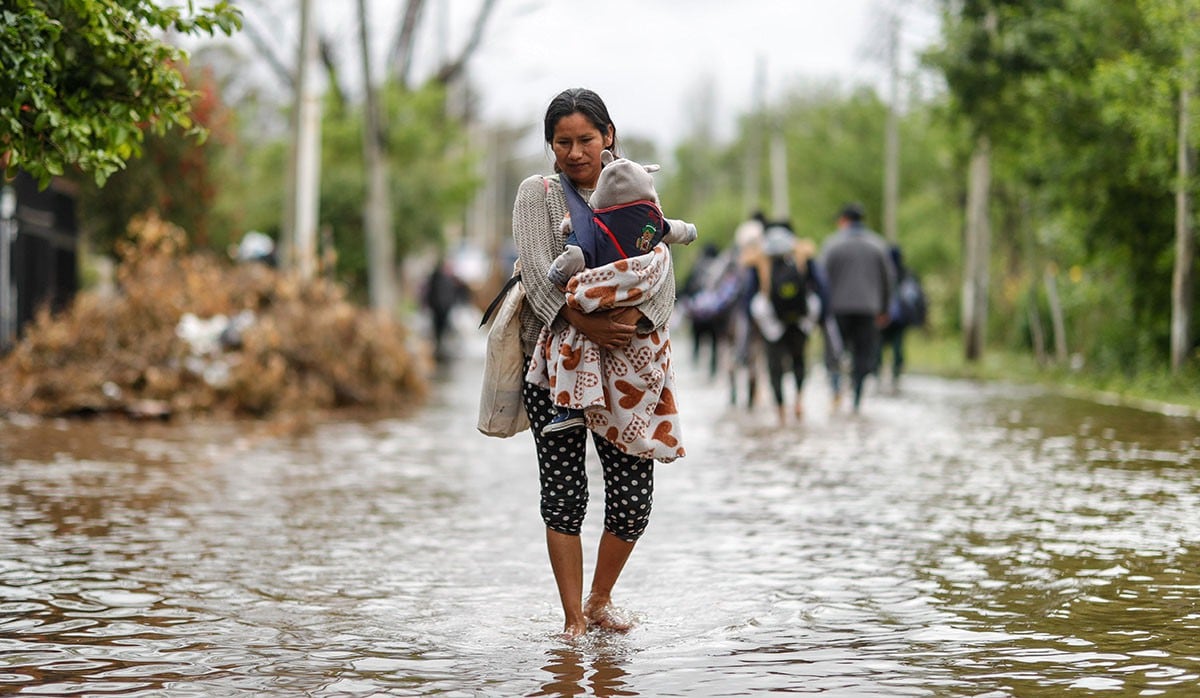 Una mujer sostiene un niño mientras camina por una de las calles inundada por la fuerte lluvia en esta región. (Foto: EFE)