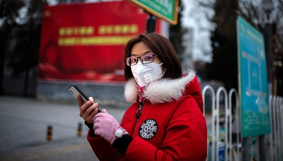 Una mujer con una máscara protectora para protegerse contra el coronavirus COVID-19 navega por su teléfono mientras está parada en una bicicleta (no representada) en una luz roja en una calle en Beijing. (Foto: AFP)