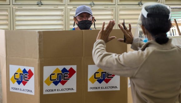 Un trabajador electoral ayuda a un votante a emitir su voto medidas de distanciamiento sanitario en una mesa de votación en una escuela en Caracas, el 6 de diciembre de 2020 durante las elecciones legislativas de Venezuela. (Cristian Hernandez / AFP)
