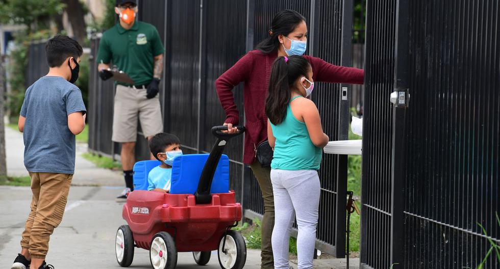 Imagen referencial de abril 2020. Una mujer con sus hijos con máscaras se estira para recoger una bolsa de comestibles distribuidos en un banco de alimentos abierto en respuesta a la pandemia de coronavirus. (AFP/ Frederic J. BROWN).