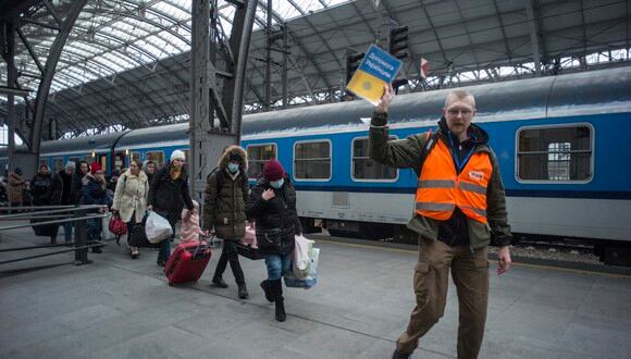 Un voluntario que sostiene un cartel que dice "Ayuda a los ucranianos" lidera el camino seguido por refugiados de Ucrania que llegan a la estación principal de tren en Praga, República Checa. (Foto: Michal Cizek / AFP)