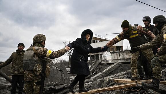 Una mujer es asistida por militares ucranianos mientras la gente cruza un puente destruido mientras evacuan la ciudad de Irpin, al noroeste de Kiev. (Foto de Aris Messinis / AFP)