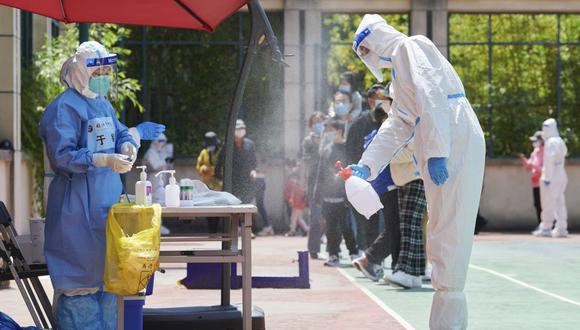 Un voluntario de la comunidad que usa equipo de protección personal desinfecta un área antes de realizar una prueba del coronavirus Covid-19 en un recinto durante un cierre de Covid-19 en el distrito de Pudong en Shanghái el 17 de abril de 2022. (Foto de LIU JIN / AFP)