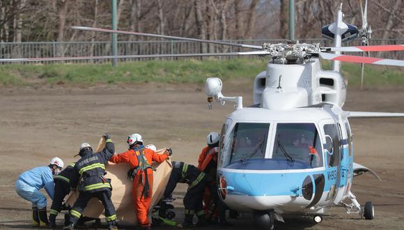 El personal de rescate sostiene material para proteger una camilla de los medios, mientras hacen una transferencia de un helicóptero a una ambulancia que espera en un campo escolar en Shari, subprefectura de Okhotsk de Hokkaido el 24 de abril de 2022. (Foto de JIJI PRESS / AFP)