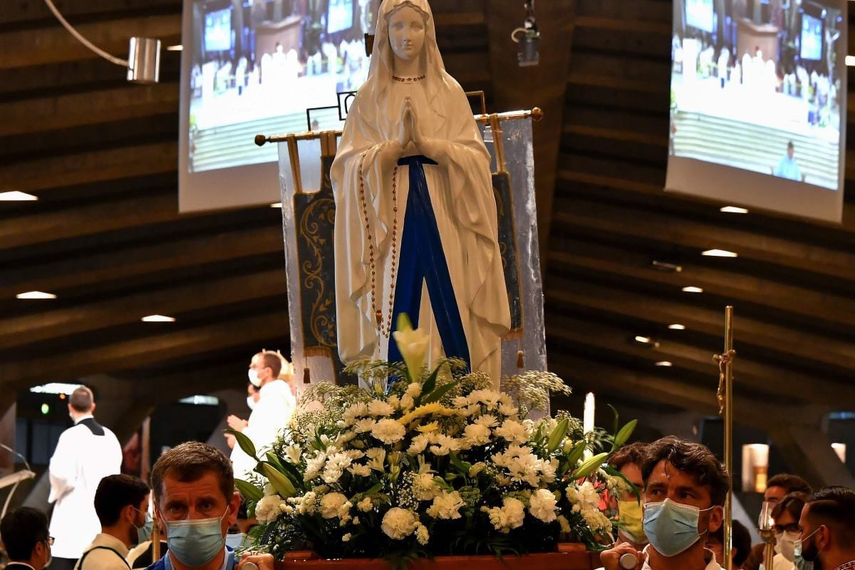 Fieles con mascarillas llevan una estatua de la Virgen María durante una misa en la Basílica de Saint Pie X en Lourdes (Francia). (AFP / GEORGES GOBET).