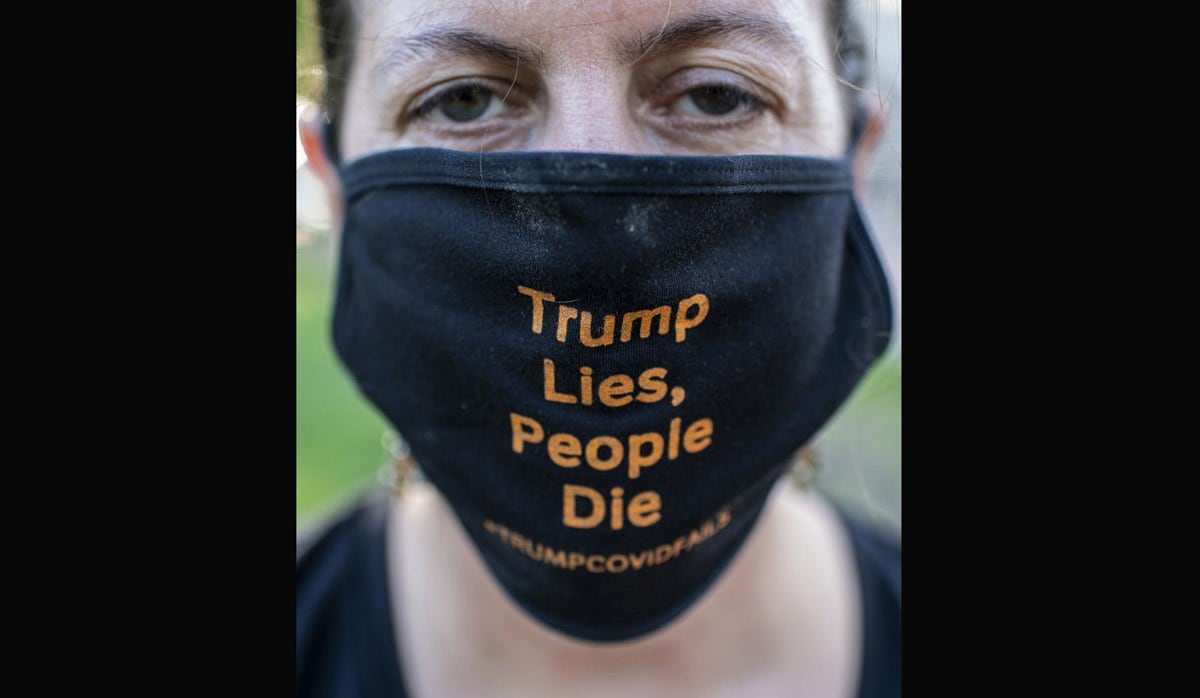 Un manifestante con una máscara facial que dice "Trump miente, la gente muere" posa mientras muestra bolsas de cadáveres falsas durante una protesta frente a la Casa Blanca en Washington, DC. (Foto: AFP/Eric BARADAT)
