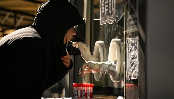 Un trabajador de la salud toma una muestra de hisopo de un hombre para realizarle la prueba del coronavirus Covid-19 en un sitio de recolección de hisopos en Beijing el 11 de diciembre de 2022. (Foto de Noel CELIS / AFP)