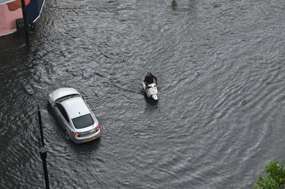 Según las autoridades, en varias zonas del sur de Inglaterra podrían caer hasta 100 milímetros de lluvia en pocas horas, el doble de la media mensual para un mes de julio. En la foto, un automóvil y una motocicleta atraviesan una carretera inundada en el distrito de The Nine Elms de Londres. (Texto: AFP / JUSTIN TALLIS / AFP)