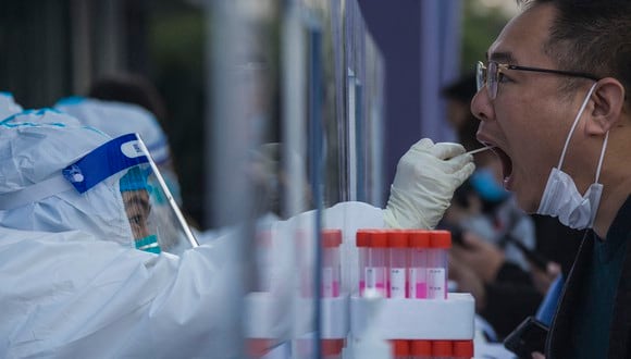 Un trabajador de la salud toma una muestra de un hisopo de un hombre para detectar el Covid-19 durante una prueba masiva en un centro de pruebas improvisado en el este de China. (Foto: AFP)