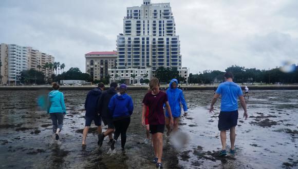 La gente camina a lo largo de las marismas mientras la marea retrocede desde la Bahía de Tampa antes de que el huracán Ian toque tierra el 28 de septiembre de 2022 en Tampa, Florida. (Foto de Bryan R. Smith / AFP)