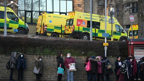 La gente espera en una parada de autobús debajo de las ambulancias estacionadas frente al hospital Bradford Royal Infirmary en Bradford, norte de Inglaterra, el 5 de enero de 2022.  (Foto de Oli SCARFF / AFP)