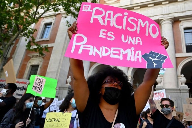 Una manifestante sostiene un cartel que dice "el racismo es una pandemia" en Madrid, España, durante una manifestación en memoria de George Floyd, quien murió luego de que un policía se arrodillara sobre su cuello en una intervención. (AFP / Gabriel BOUYS)
