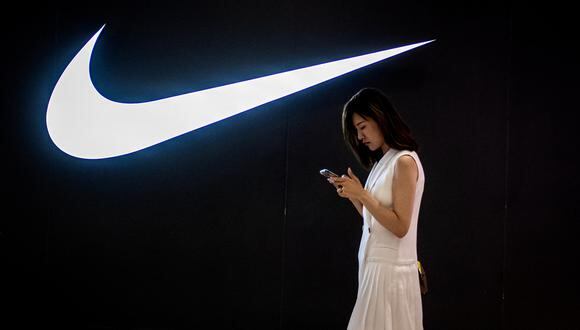 Una mujer mira su teléfono mientras pasa junto a un logotipo de Nike dentro de un centro comercial en Beijing el 2 de junio de 2021. (Foto de NICOLAS ASFOURI / AFP)