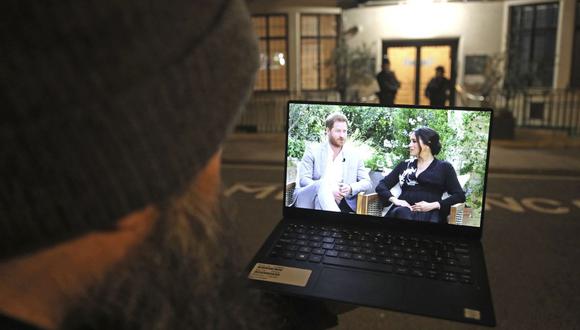 Un hombre mira su computadora portátil que muestra una entrevista del príncipe Harry y Meghan fuera del Hospital King Edward VII, en Londres, el 8 de marzo de 2021. (Yui Mok/PA/AP).