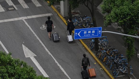 Los residentes del vecindario caminan con su equipaje en una calle antes de abordar un automóvil durante un encierro de Covid-19 en el distrito de Jing'an en Shanghai el 30 de abril de 2022. (Foto de Hector RETAMAL / AFP)
