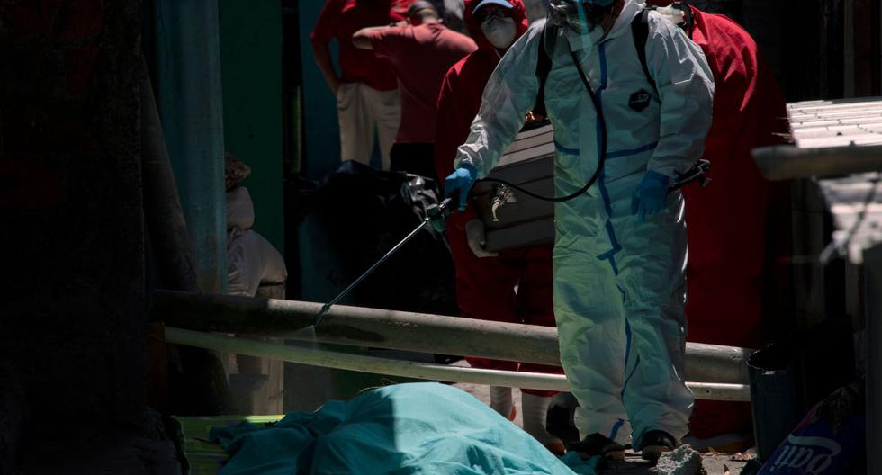Funerarias y trabajadores de la salud vestidos con trajes de bioseguridad desinfectan el cuerpo de un hombre de 75 años que murió, presuntamente víctima de COVID-19. (AFP/Yuri CORTEZ).