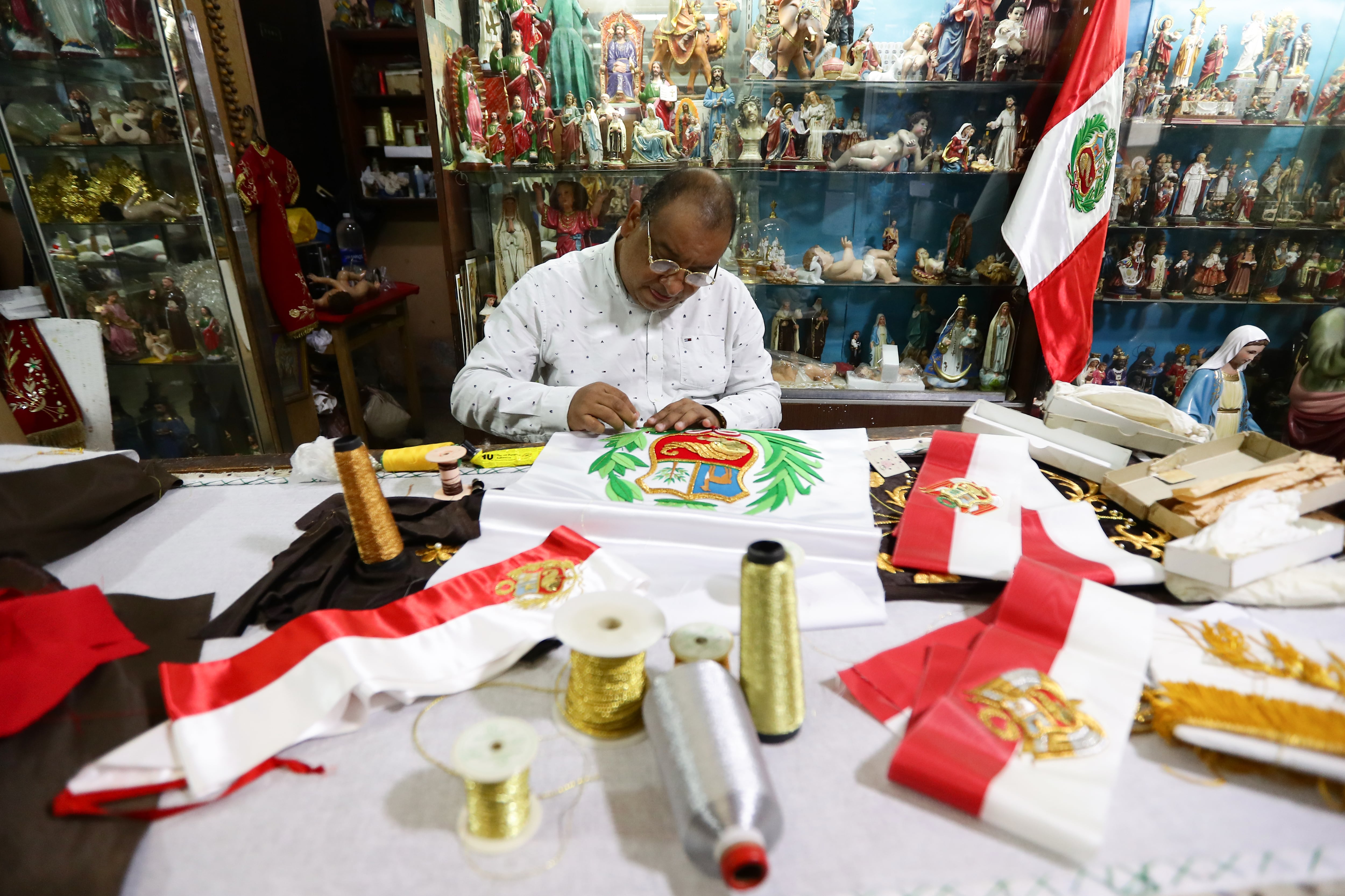 Dante Grados trabaja desde su adolescencia junto a su padre realizando banderas, bandas presidenciales y fajines ministeriales. Ahora con 61 años y una familia al lado, sigue la tradición que heredó de su familia. Tras él se encuentra la última bandera que confeccionó su padre antes de fallecer hace unos 6 años aproximadamente.
Fotos: Jesús Saucedo / @photo.gec