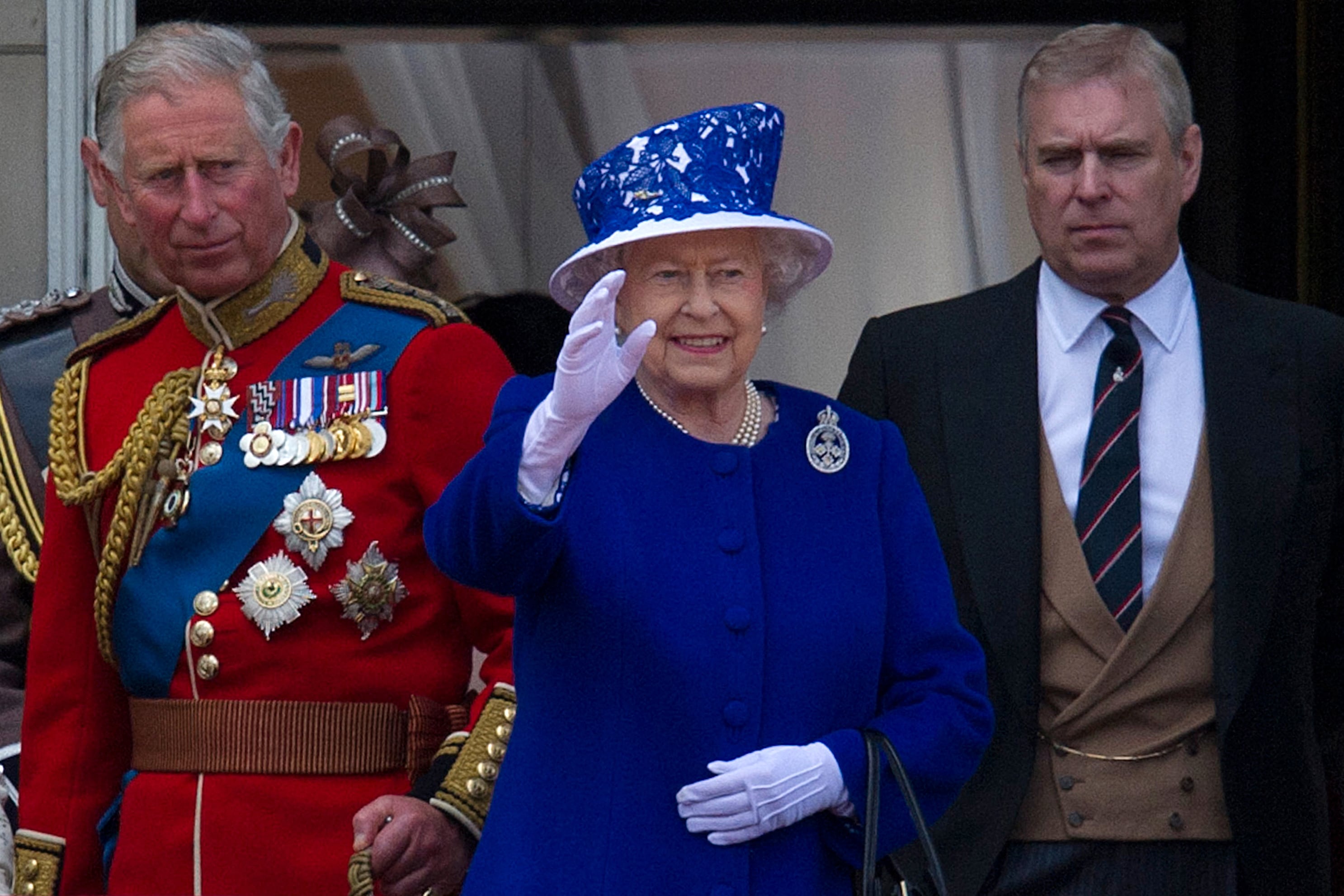 La reina Isabel II (centro) saluda desde el balcón del Palacio de Buckingham, flanqueada por sus hijos, el príncipe Carlos (izq.) y el príncipe Andrés, el 15 de junio de 2013. (Foto de CARL COURT / AFP).
