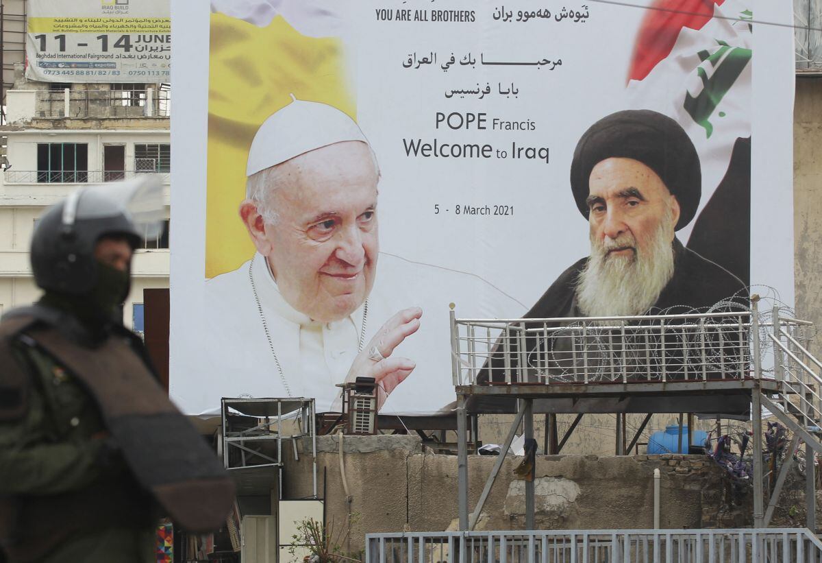 Un guardia de seguridad iraquí se para frente a una enorme valla publicitaria con retratos del Papa Francisco y el Gran Ayatola Alí Sistani en el centro de Bagdad. (Foto de AHMAD AL-RUBAYE / AFP).