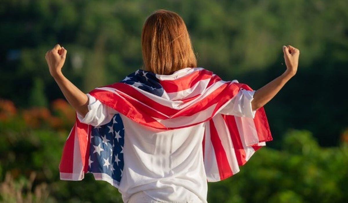 Una mujer con la bandera de Estados Unidos en su espalda muy feliz y orgullosa de vivir en el país norteamericano (Foto: Freepik)