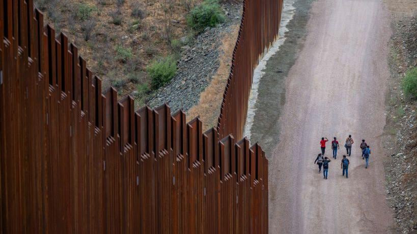 Migrantes procedentes de Centroamérica y Sudamérica, que buscan asilo, caminan junto a la valla fronteriza tras haber cruzado ilegalmente hacia Estados Unidos.