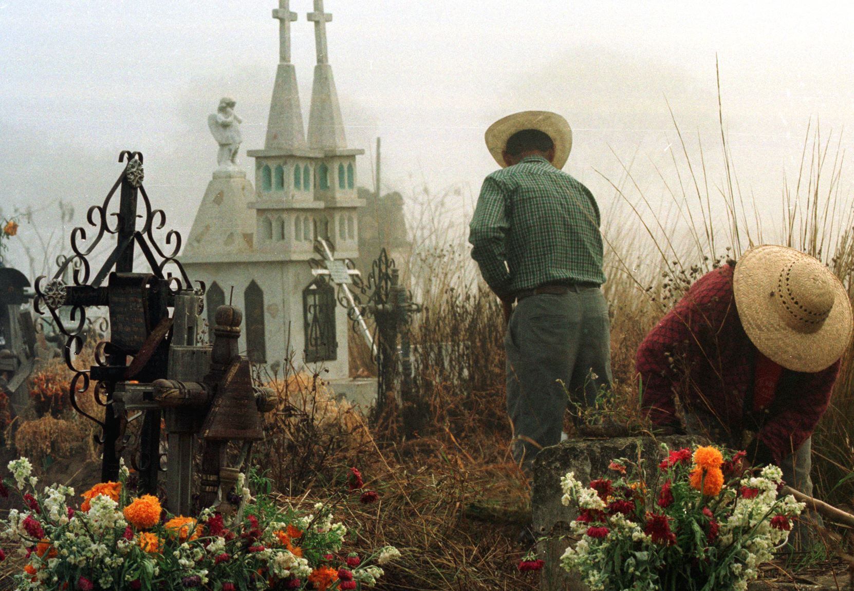 Una pareja prepara las tumbas de un par de parientes en el cementerio de Libres, en el Estado mexicano de Puebla, el 01 de noviembre de 1999 para las tradicionales celebraciones del Día de los Muertos. (Foto por JORGE SILVA / AFP)