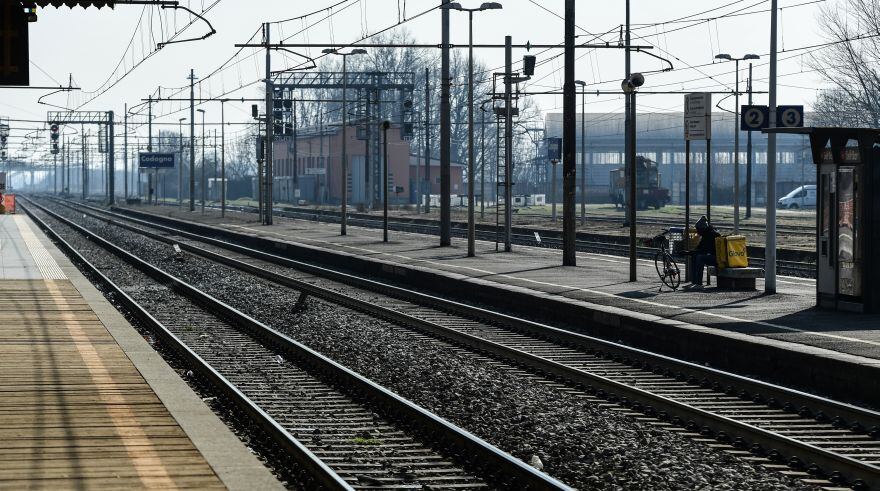 Una vista general muestra a un hombre que trabajaba para un servicio de entrega sentado en su bicicleta en una plataforma de la estación de ferrocarril desierta en Codogno, al sureste de Milán, el 22 de febrero de 2020. (Photo by Miguel MEDINA / AFP)