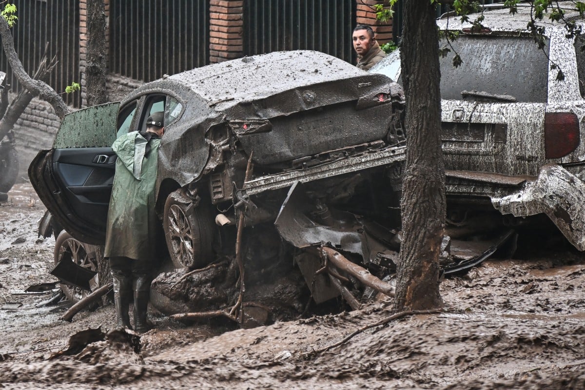 Personas inspeccionan vehículos dañados y cubiertos de barro tras un deslizamiento de tierra en el distrito de Las Condes, Santiago, el 8 de octubre de 2026. (RODRIGO ARANGUA / AFP)