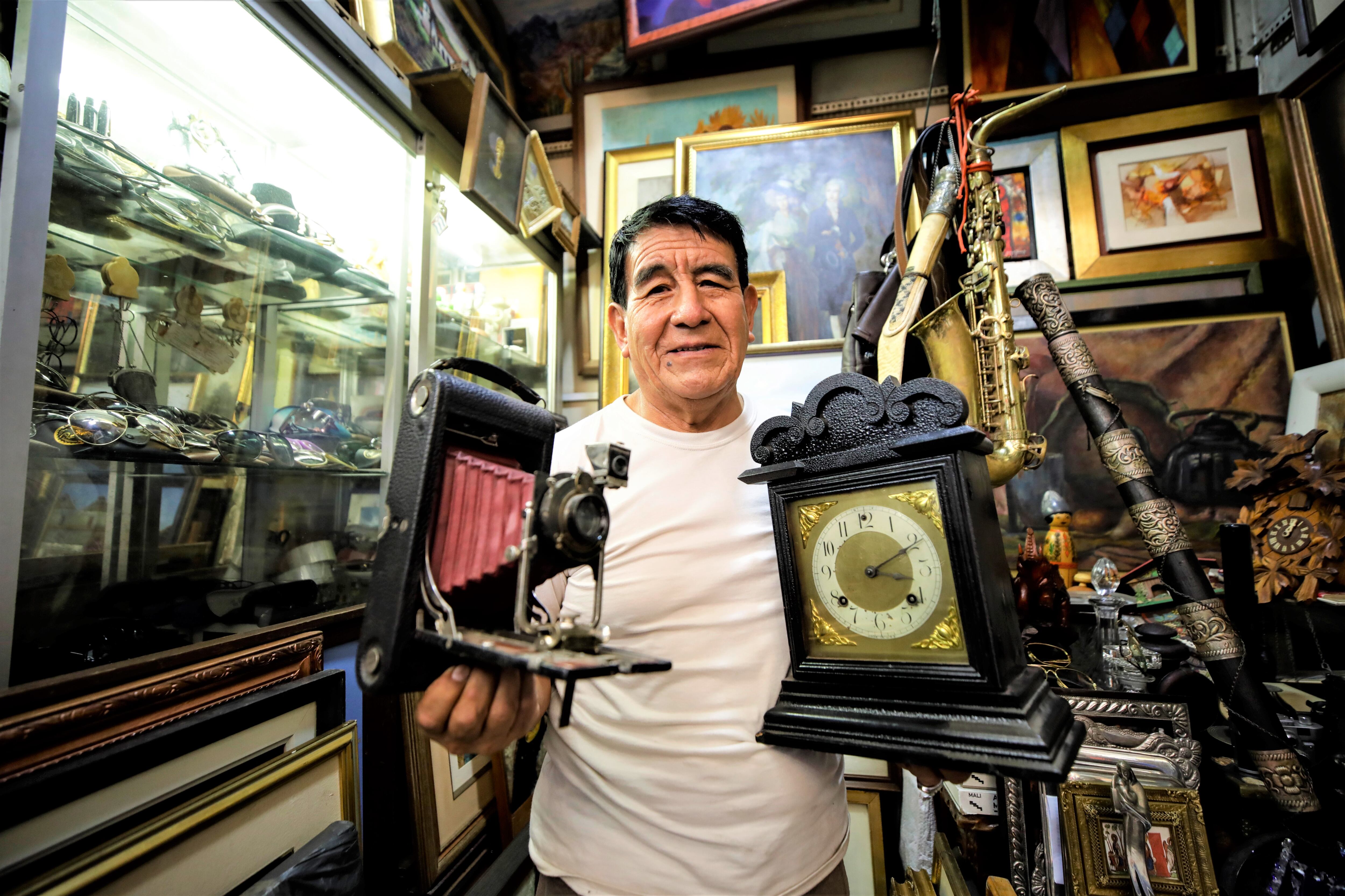 Vendedor mostrando las reliquias que oferta: Una cámara de los años 30 y un reloj Ansonia.