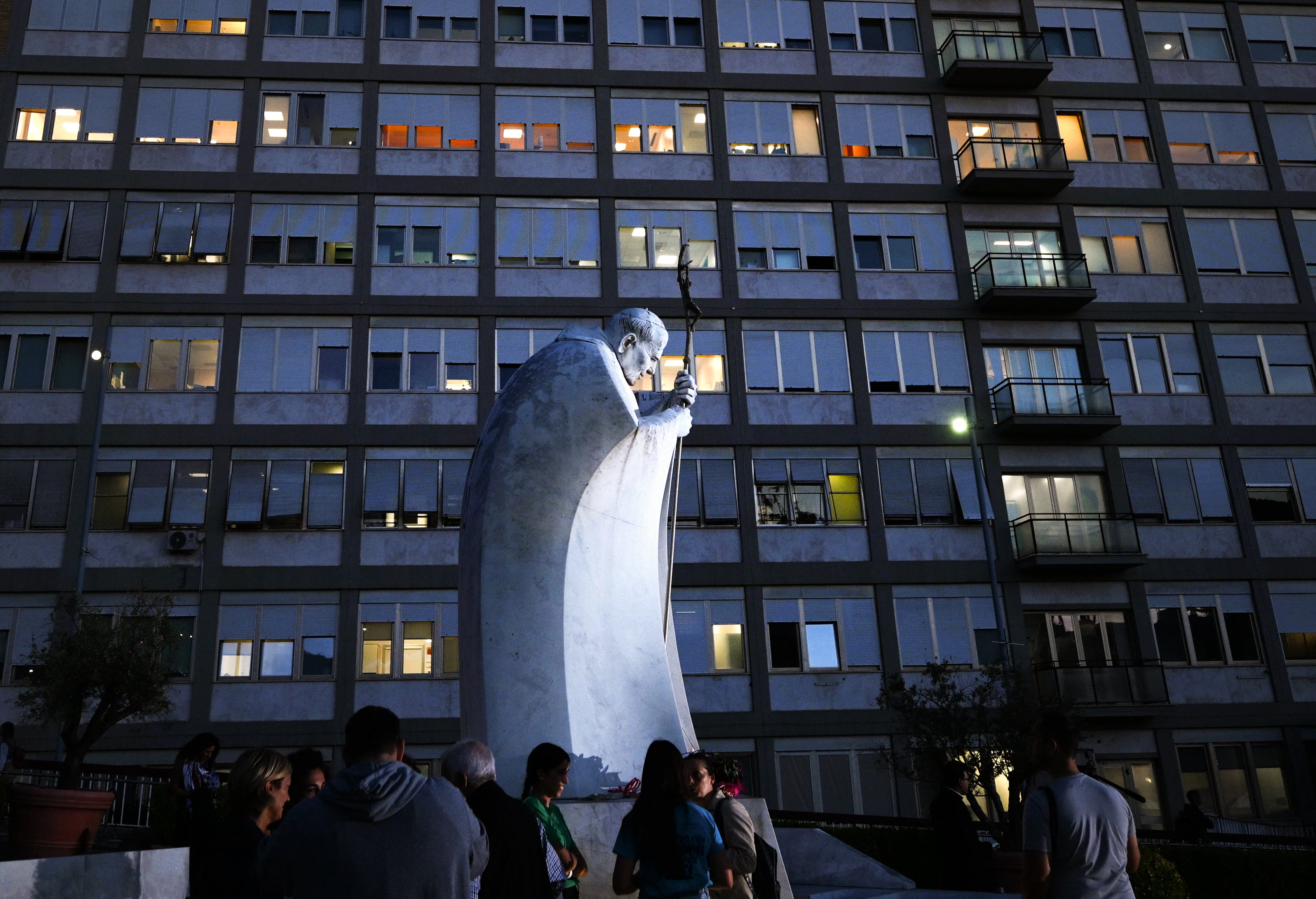 Varias personas rezan ante la estatua de Juan Pablo II a las afueras del Hospital Universitario Gemelli, donde el Papa León XIV se recupera tras someterse a una operación para extirparle un tumor canceroso del pulmón derecho. (Foto de Tiziana FABI / AFP).