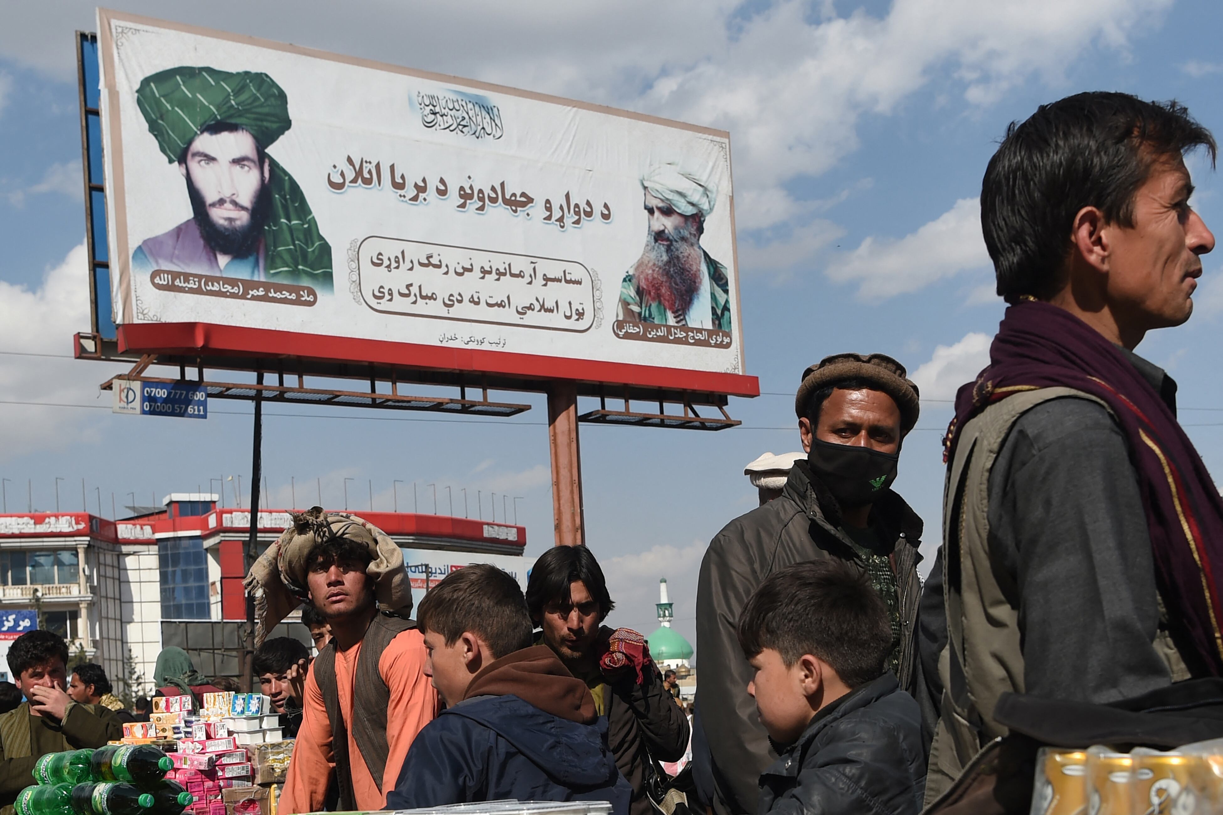 Los vendedores trabajan en un mercado cerca de una valla publicitaria que muestra al fundador de los talibanes y difunto líder supremo Mullah Omar (L) y difunto líder de la red militante Haqqani Jalaluddin Haqqani (R) cerca de la mezquita Pul-e Khishti en Kabul el 1 de marzo de 2022. ( Foto de Wakil KOHSAR / AFP)